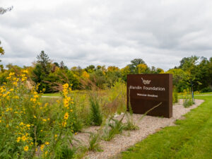 Blandin Foundation Welcome / Boozhoo sign outside on a path with wildflowers