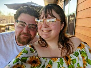 photo of Shaylee Erdmann smiling with their partner, taken outside as a selfie